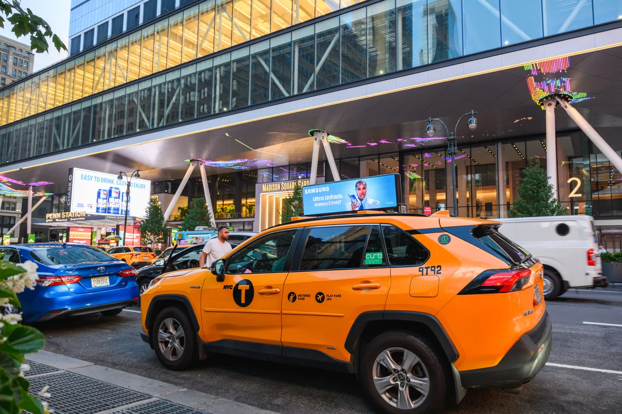 Samsung digital taxi top outside Madison Square Garden and the Penn Station entrance, with a Bud Light digital billboard behind, New York, 2025