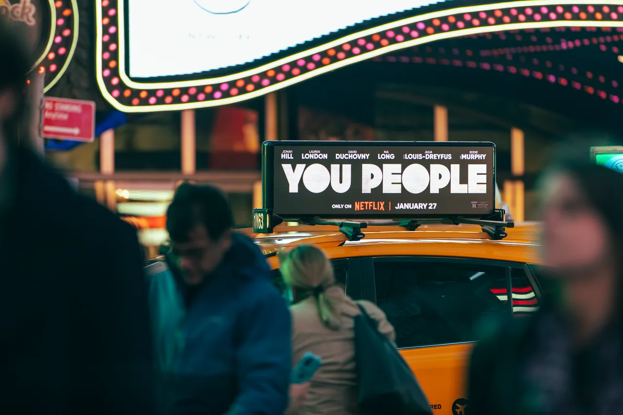 Netflix You People advertisement on a digital taxi top display at night under the Times Square marquee lights