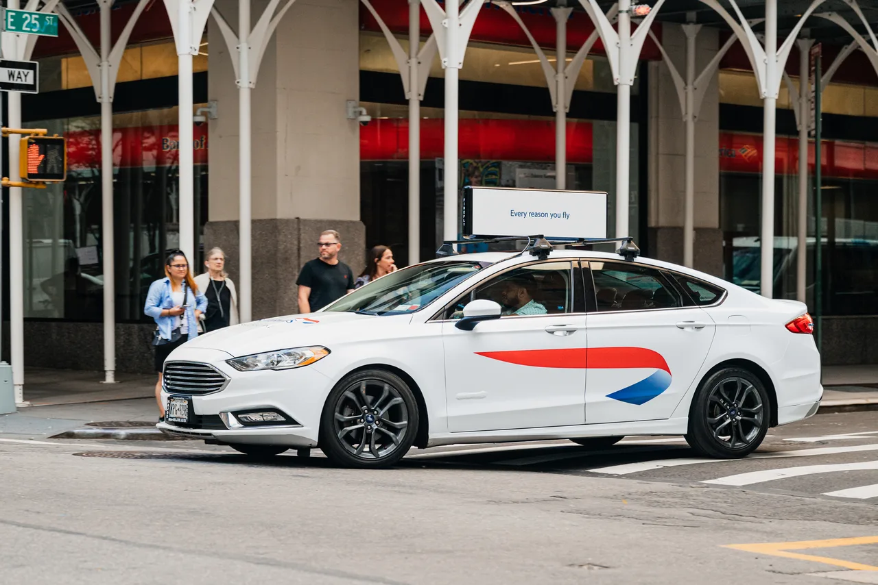 A white sedan in a British Airways 360-degree wrap crossing a Manhattan intersection