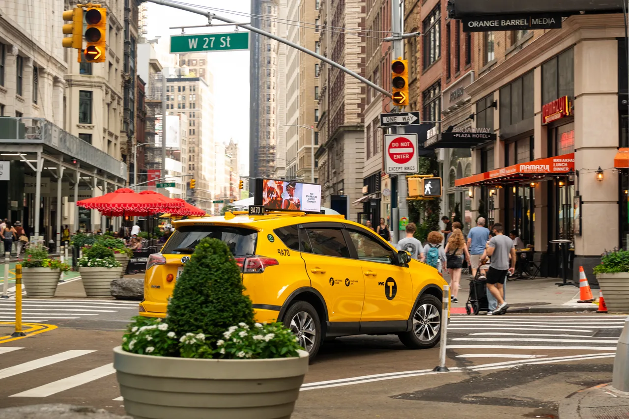 Starbucks digital taxi top on a yellow cab at Broadway and West 27th Street, NoMad, with an Orange Barrel Media wall sign on the corner building, New York, 2024