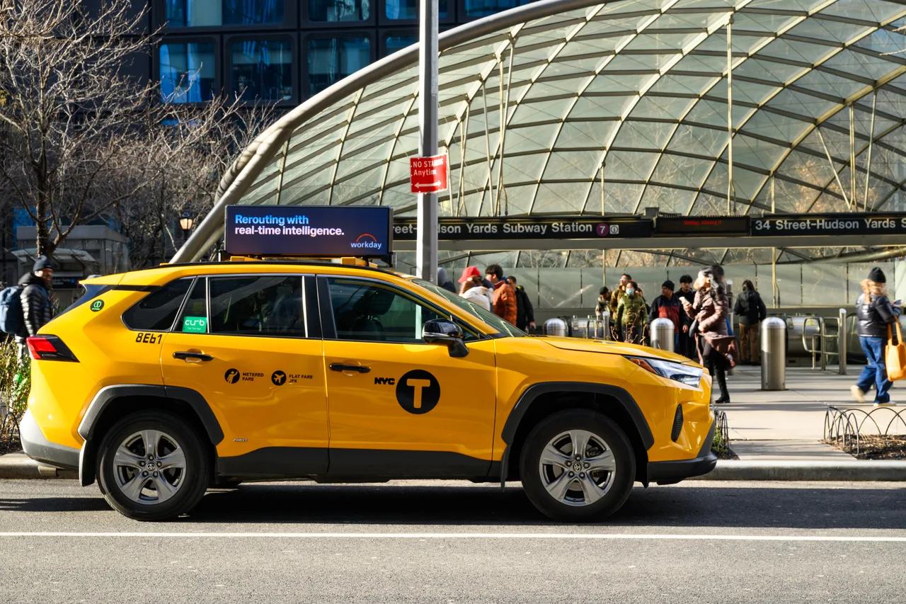 Workday digital taxi top passing the 34 St-Hudson Yards subway station entrance on the 7 line, New York, 2026