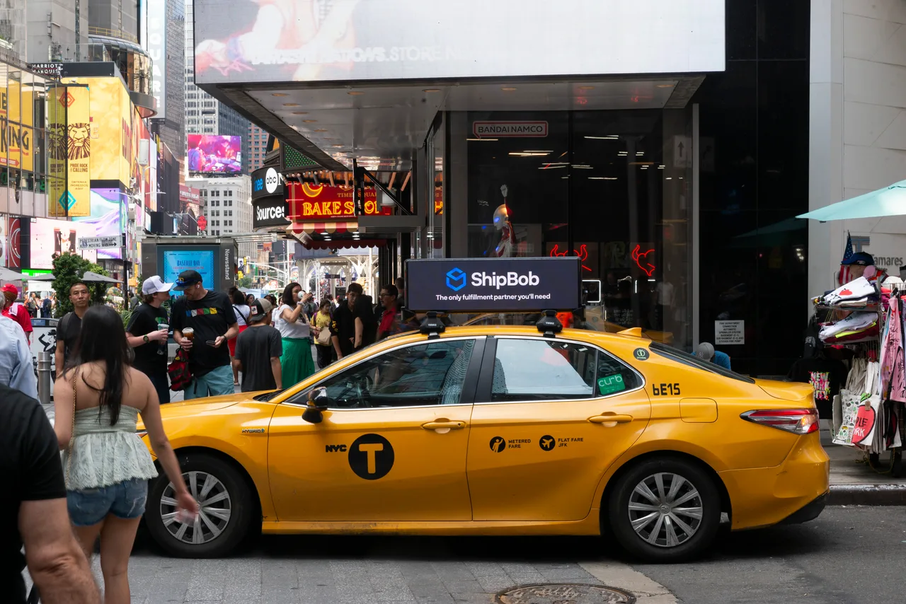 ShipBob digital taxi top on a NYC yellow cab in Times Square with the Marriott Marquis and The Lion King signs behind, 2024