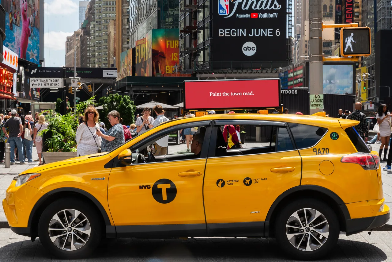 The Economist digital taxi top ad on a NYC yellow cab in Times Square, spectaculars behind, 2024